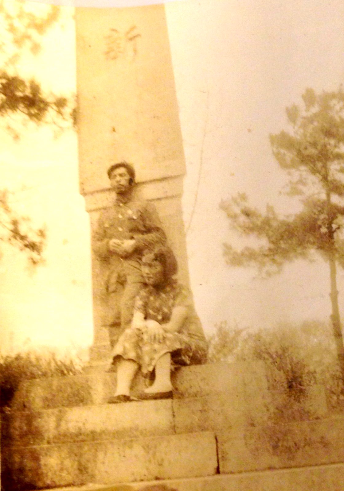 在一塊石碑前，男站立女坐在石階上目視遠方